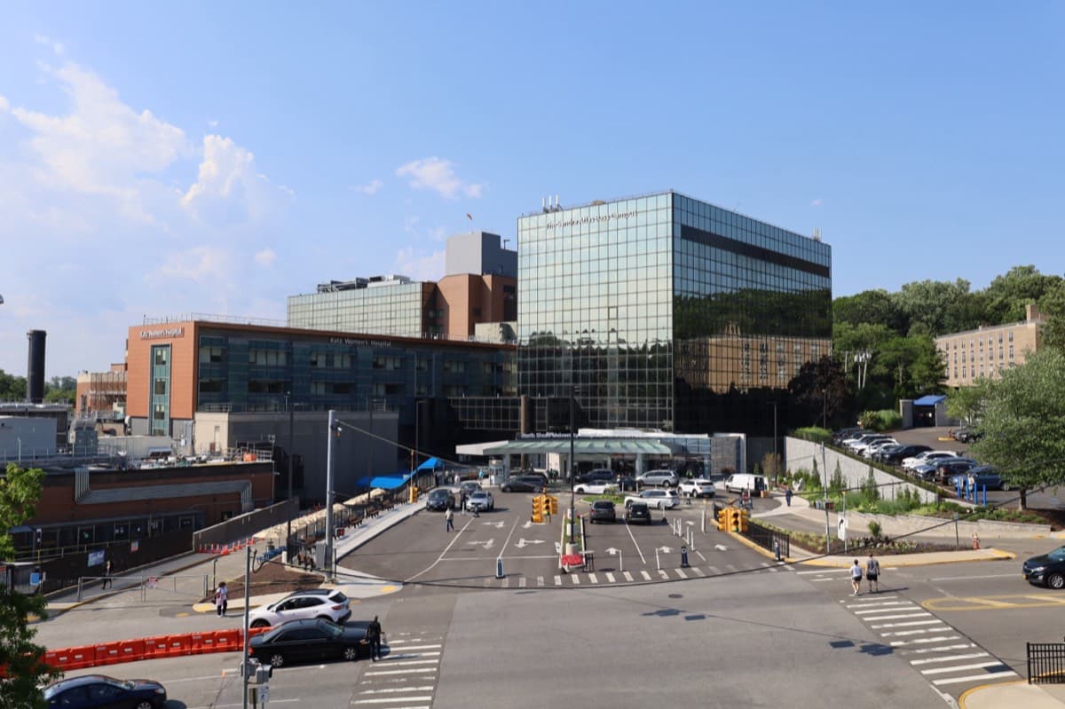 The glass tower and entrance plaza of North Shore University Hospital on a clear day.