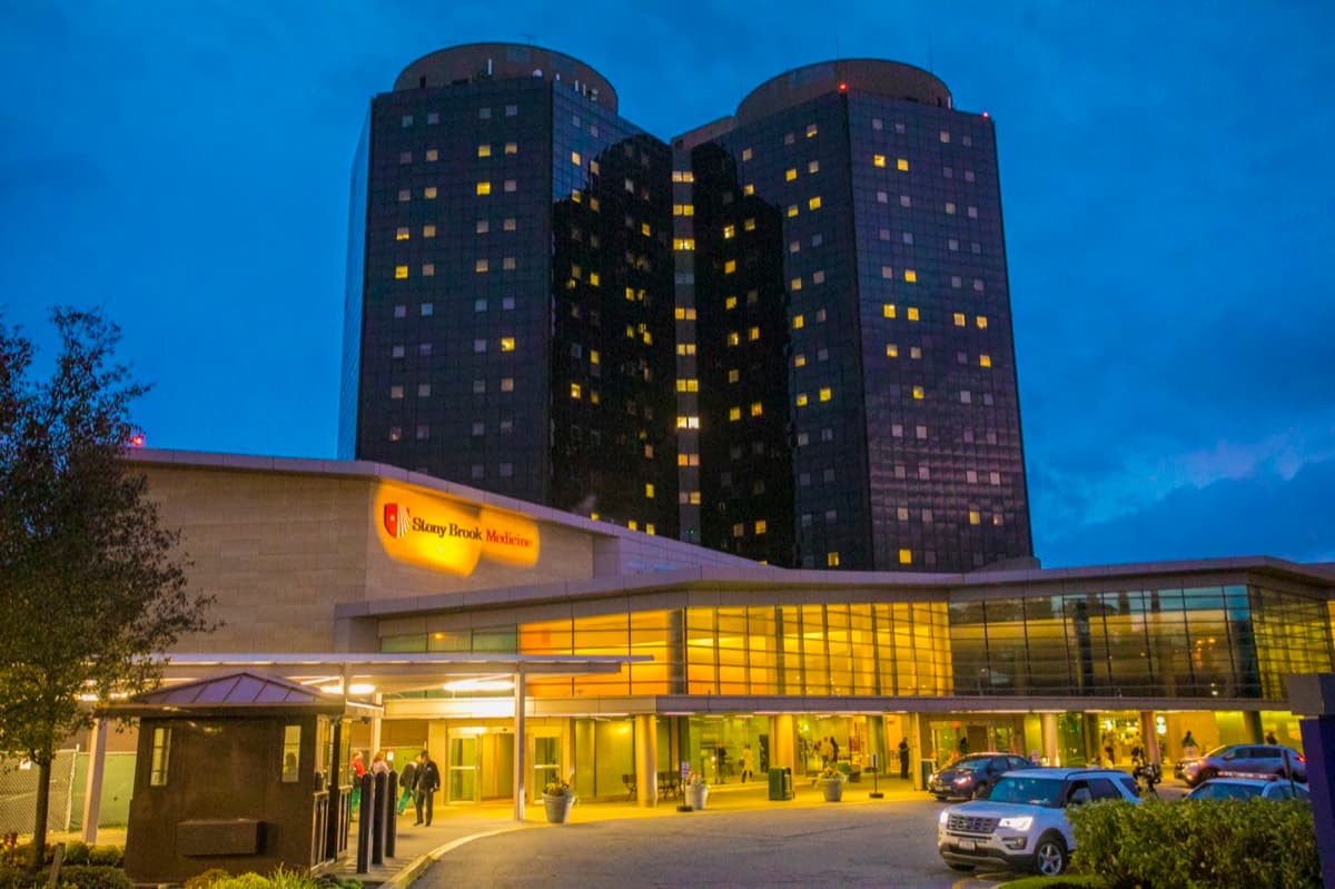 The twin towers of Stony Brook University Hospital lit up at dusk above the main entrance.
